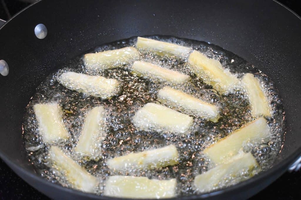 Yuca fries frying in oil in a large, black skillet.