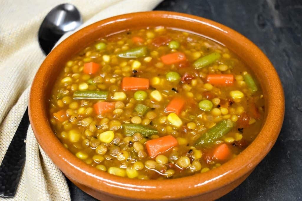 A close up picture of the lentil vegetable soup served in a red clay bowl.