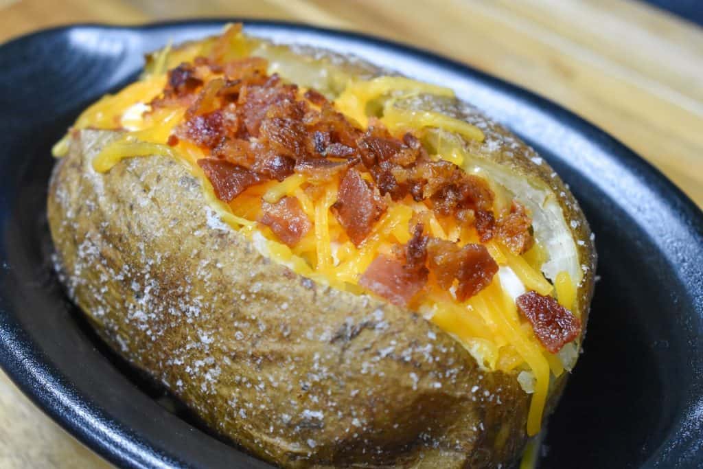 A close up image of a baked potato with melted shredded cheese and chopped bacon.