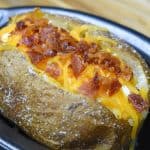 A close up image of a baked potato with melted shredded cheese and chopped bacon.