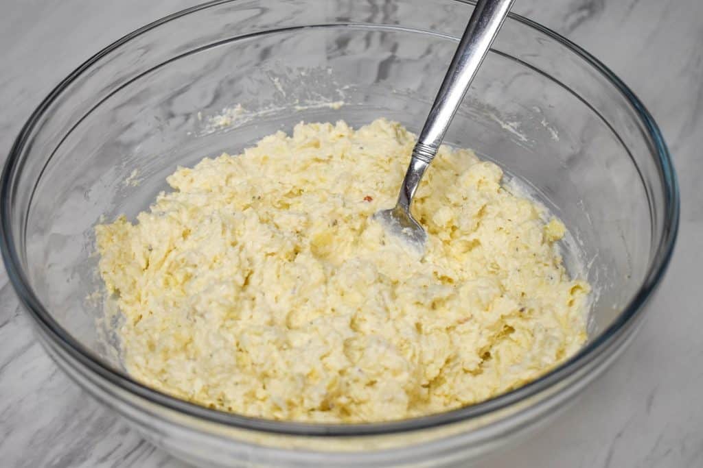 Chopped artichokes being combined with cream cheese and mayonnaise in a large, glass bowl.