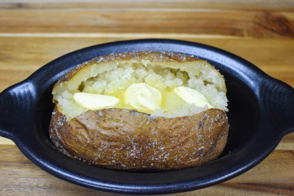 Three pats of butter melting in an opened baked potato. Served in a small black crock.