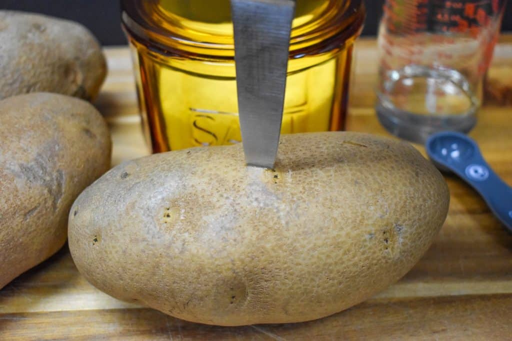 A large russet potato being pricked by a paring knife.