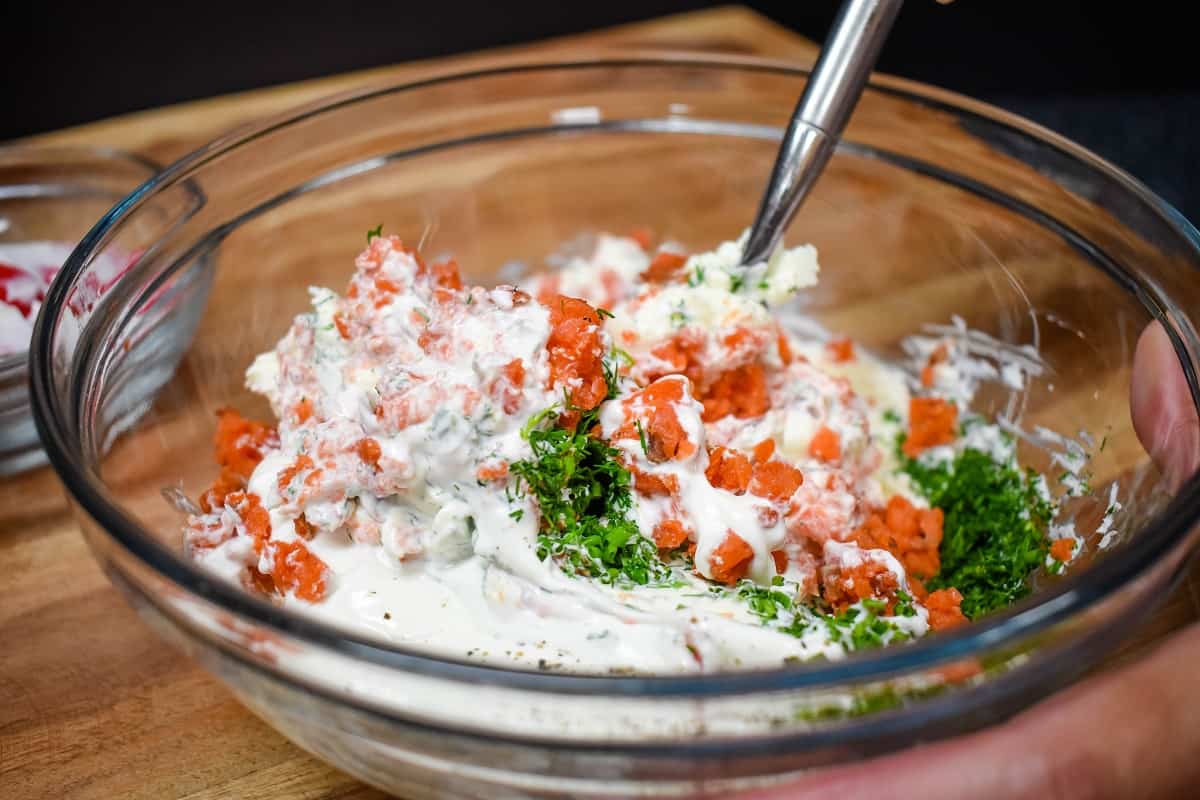 Salmon dip being stirred with a fork in a large, clear bowl.