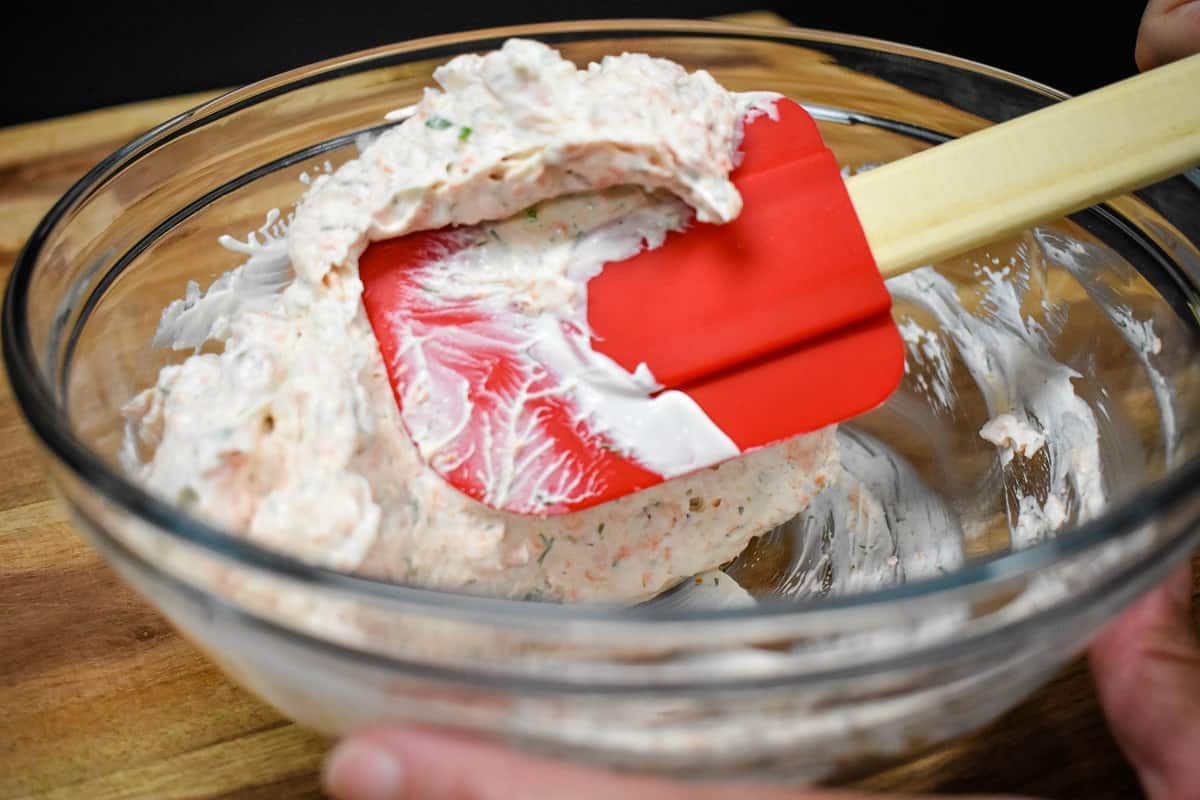Salmon dip being folded over with a red rubber spatula.