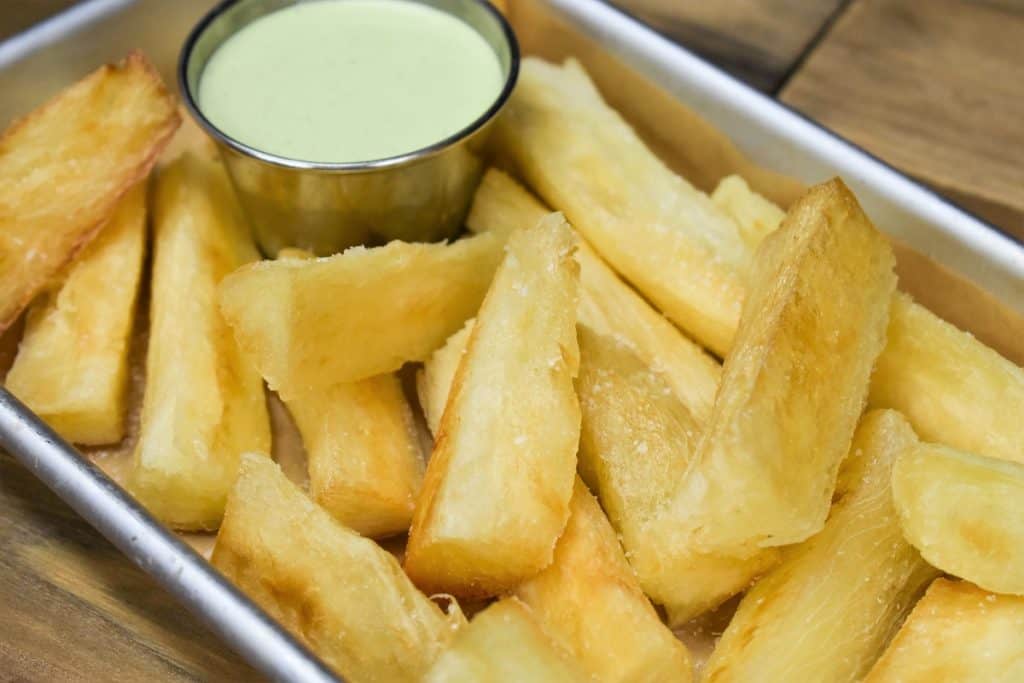 Fried yuca served with a light green cilantro sauce, served in a small metal pan.