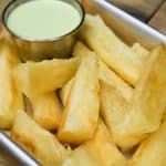 Fried yuca served with a light green cilantro sauce, served in a small metal pan.