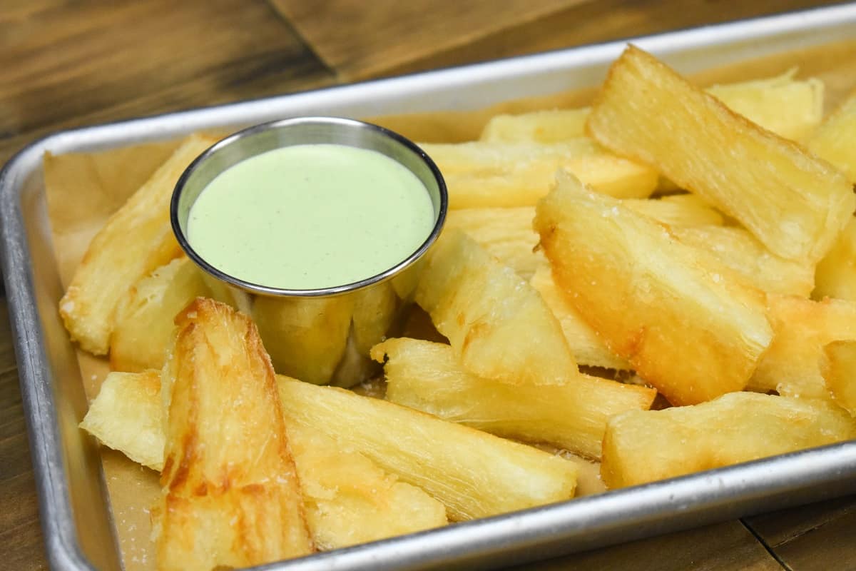 Fried yuca served with a light green cilantro sauce, served in a small metal pan.