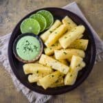 Plate of yuca frita garnished with chopped herbs, served with a green dipping sauce and lime slices on the side.