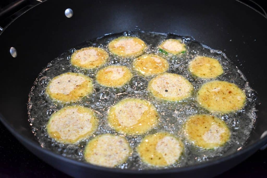 Breaded zucchini frying in a large, black skillet.