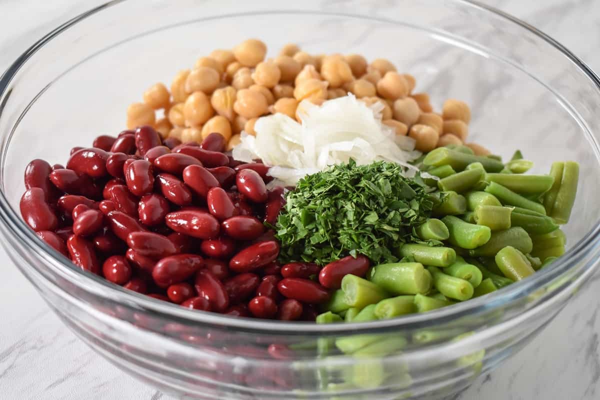 Red kidney beans, garbanzo beans, green beans, sliced onions and chopped parsley arranged in a large, glass bowl.