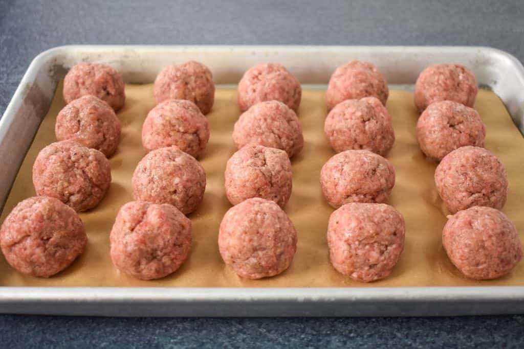 Twenty small, raw meatballs arranged on a metal sheet pan.