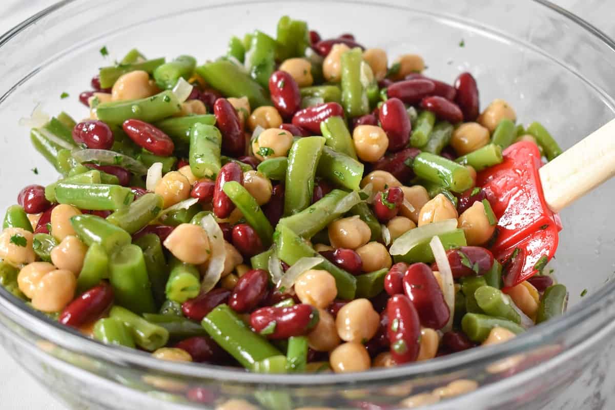 Mixed red kidney beans, garbanzo beans, green beans, sliced onions and chopped parsley in a large, glass bowl.