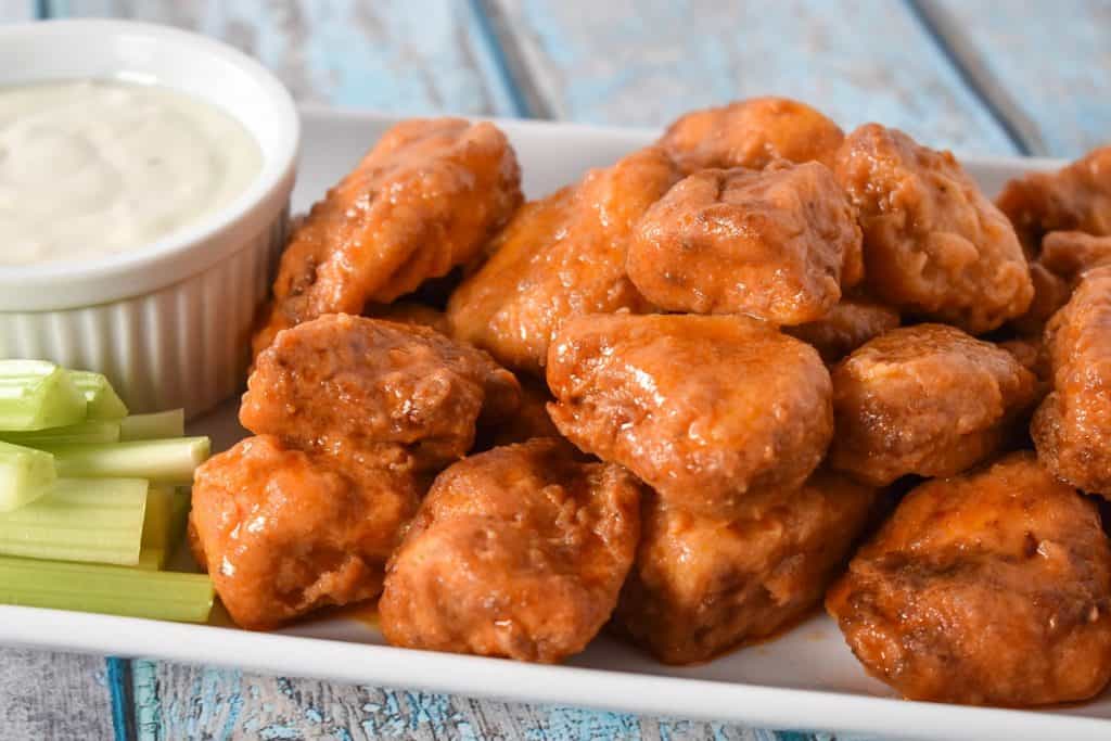 Buffalo chicken bites served on a white platter with a side of blue cheese dressing and celery sticks.