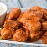 Buffalo chicken bites served on a white platter with a side of blue cheese dressing and celery sticks.