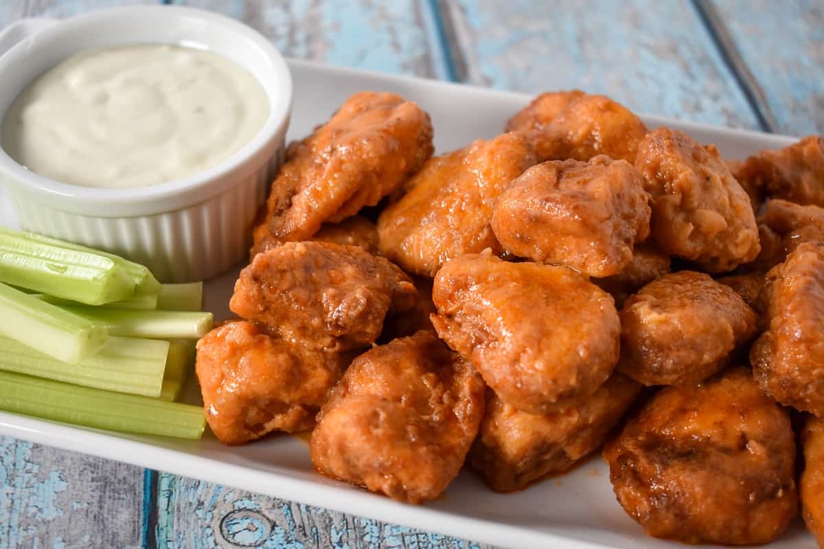 Buffalo chicken bites served on a white platter with a side of blue cheese dressing and celery sticks.