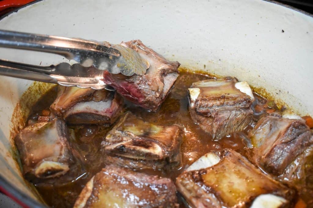 Short ribs being placed in a pot using tongs.