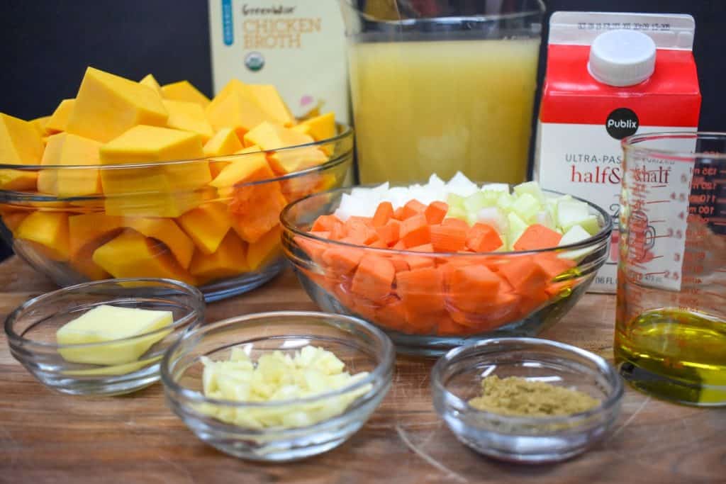 The prepped ingredients for creamy butternut squash soup arranged on a wood cutting board.