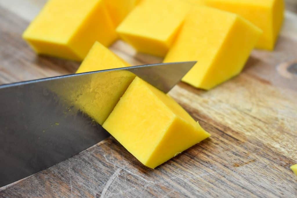 Peeled butternut squash being cut into roughly 2 inch pieces.