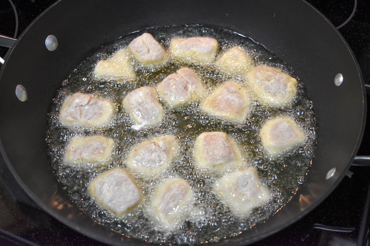 Flour coated chicken pieces frying in oil in a large, black skillet.