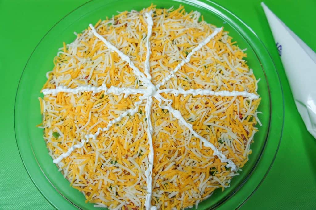 Sour cream lines on the cheese covered bean dip in a glass pie plate.