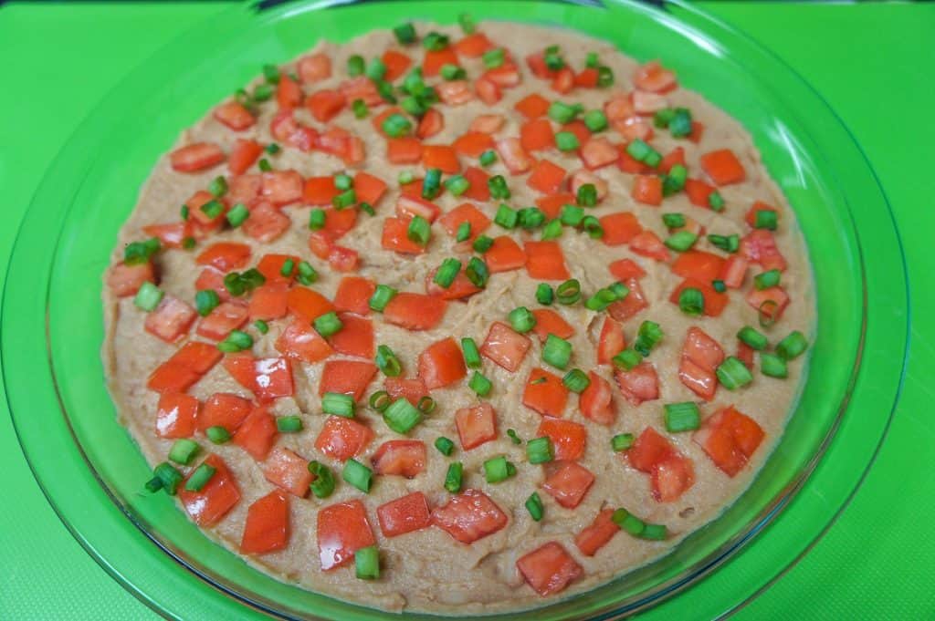 Refried beans topped with diced tomatoes and sliced green onions in a glass pie plate.
