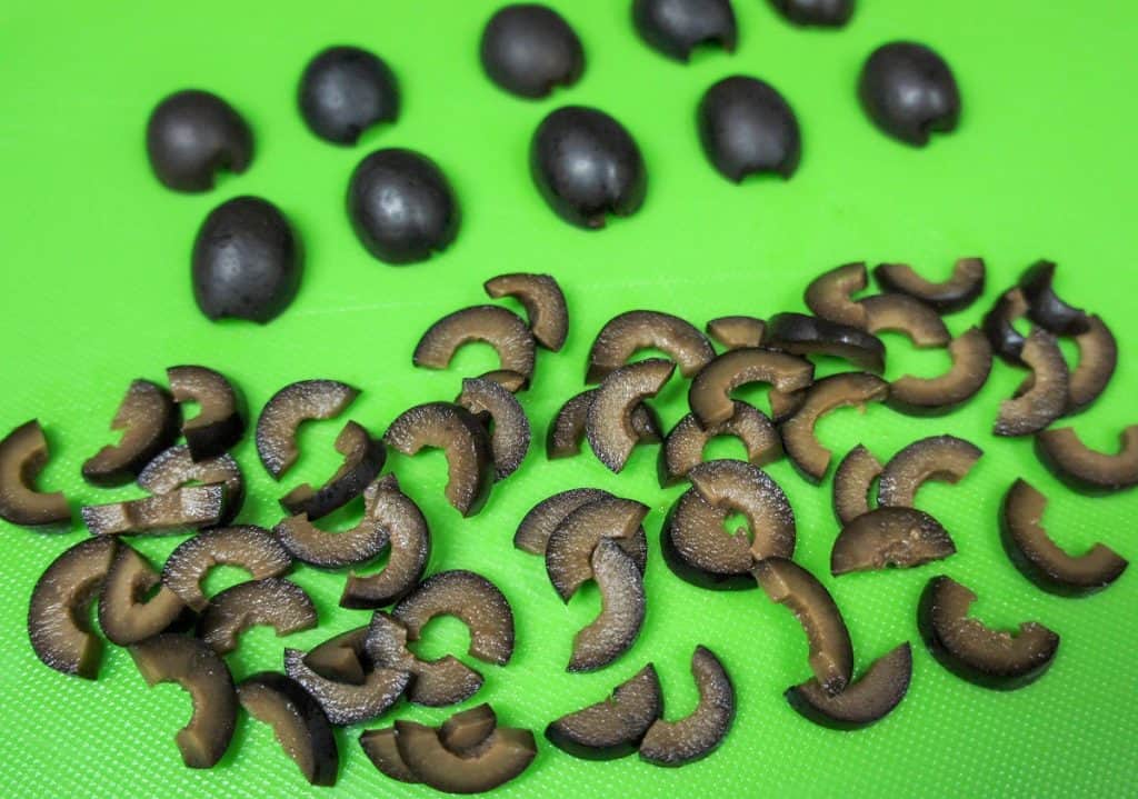 Black olive pieces displayed on a green cutting board.