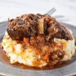 Short ribs and sauce served on a bed of mashed potatoes on a gray plate.