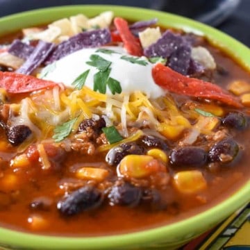 A close up image of taco soup garnished with sour cream, shredded cheese and tortilla strips.