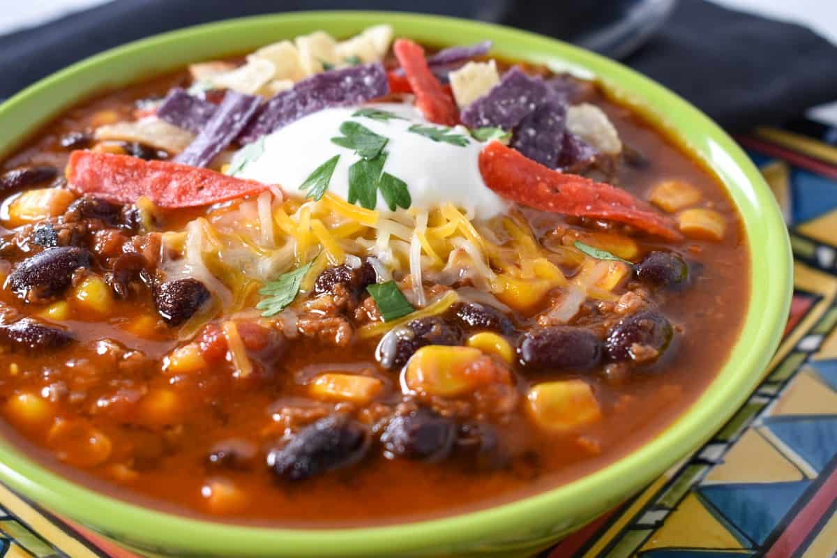 A close up image of taco soup garnished with sour cream, shredded cheese and tortilla strips.