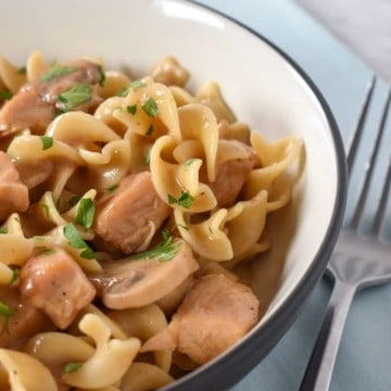 Egg noodles, cubed chicken and sliced mushrooms served in a white bowl on a light blue linen.