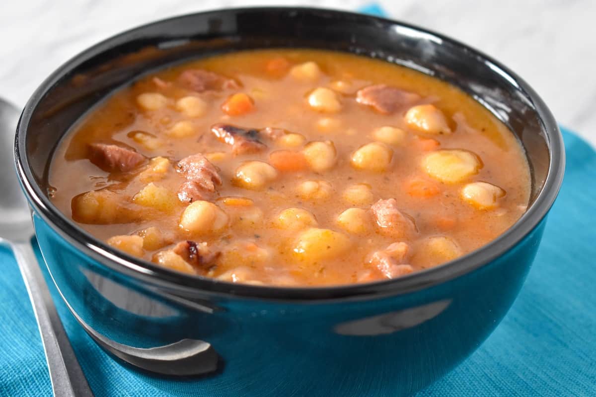 A close up image of chickpea soup served in a black bowl.