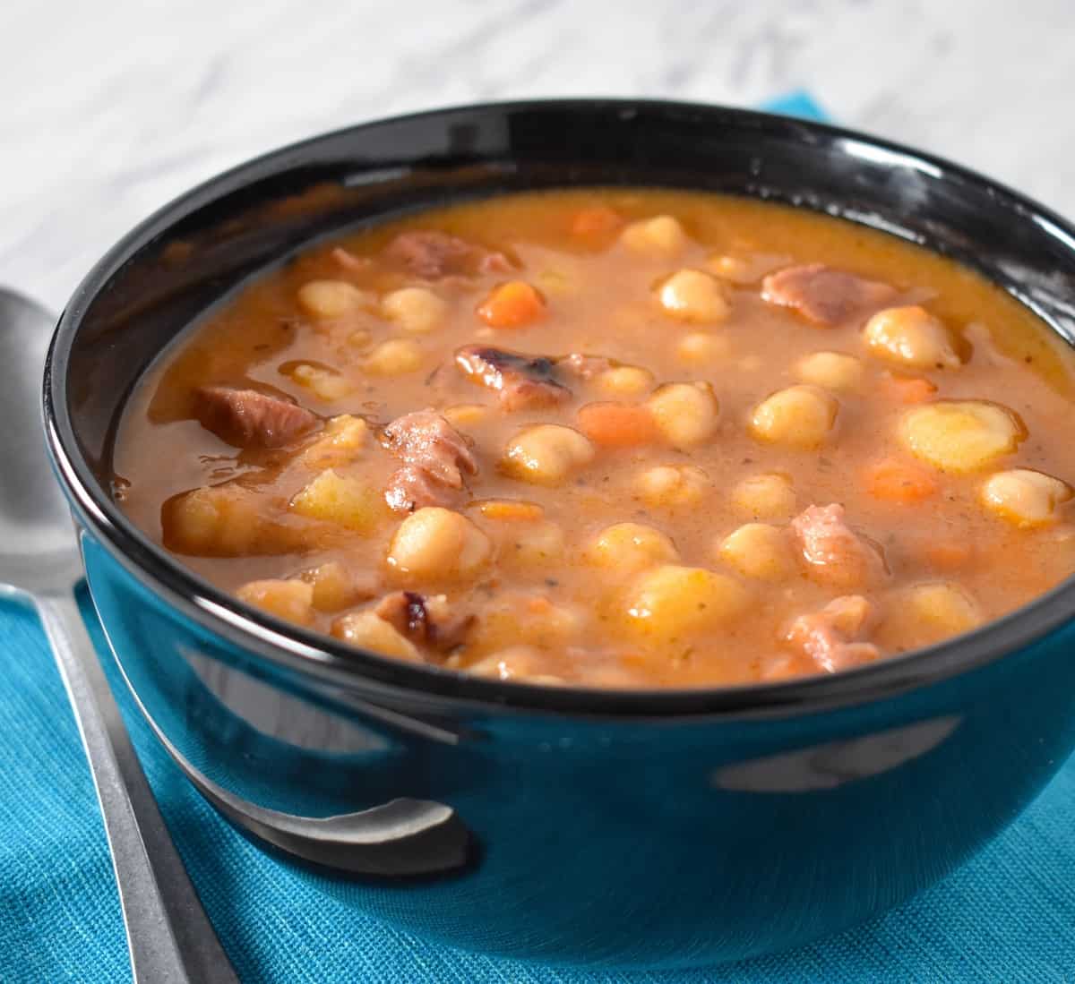 A close up image of chickpea soup served in a black bowl.