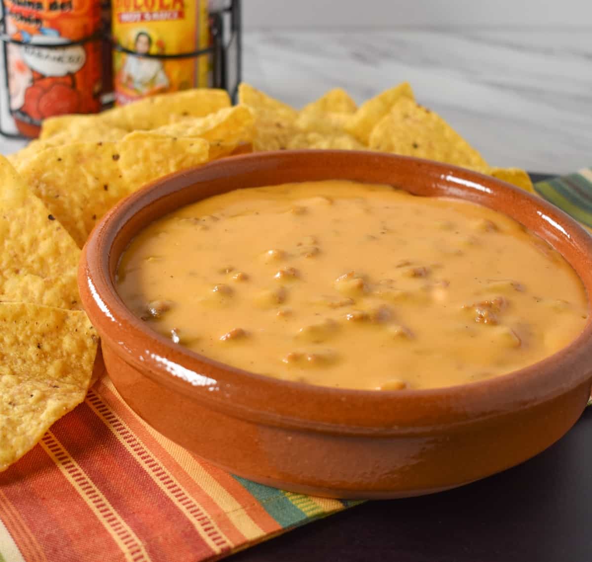 Chorizo Cheese Dip served in a terracotta crock with tortilla chips and hot sauce in the background.