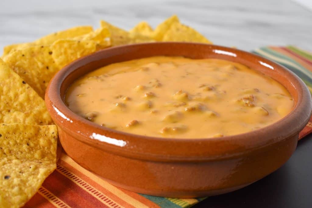 Chorizo cheese dip served in a terracotta crock with tortilla chips in the background.