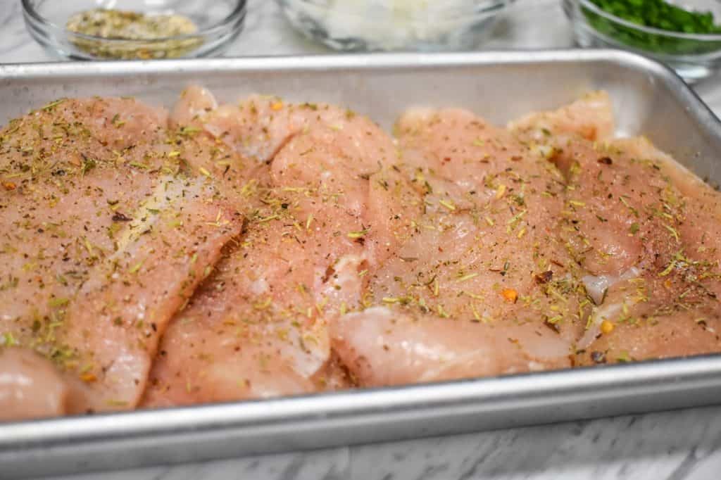 Seasoned chicken breasts on a small metal pan.