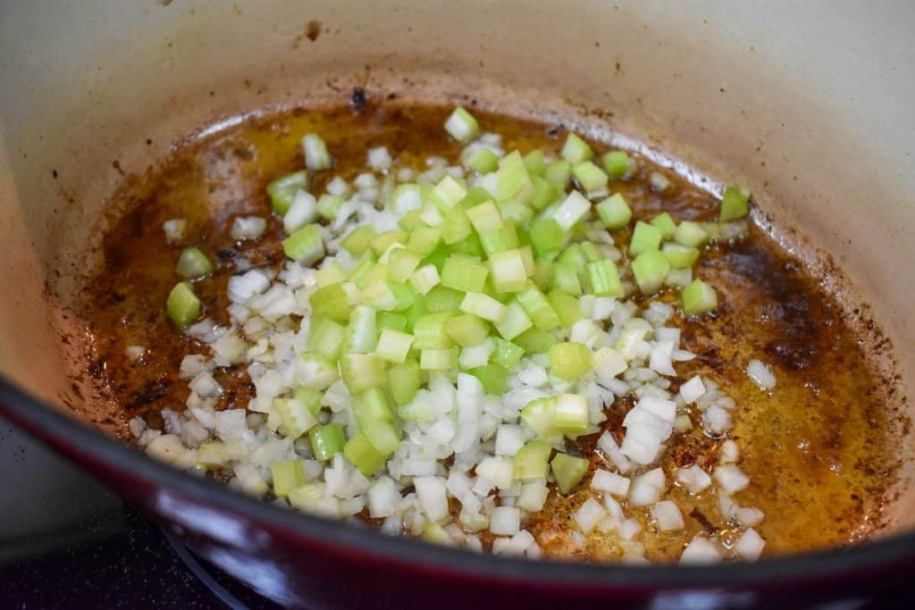 Diced onion and celery being cooked in a large, enameled cast iron pot.