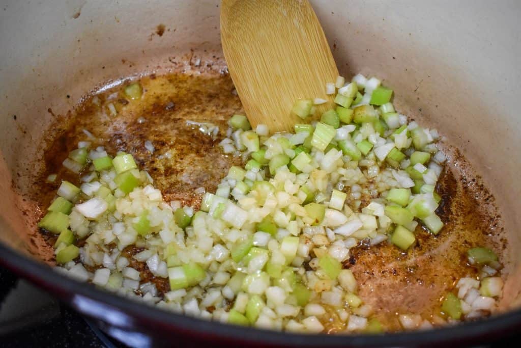 Diced onion and celery being cooked in a large, enameled cast iron pot.