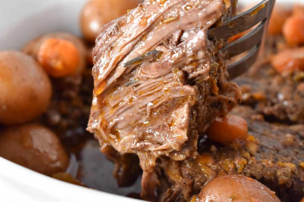 A large piece of pot roast being lifted by a serving fork.