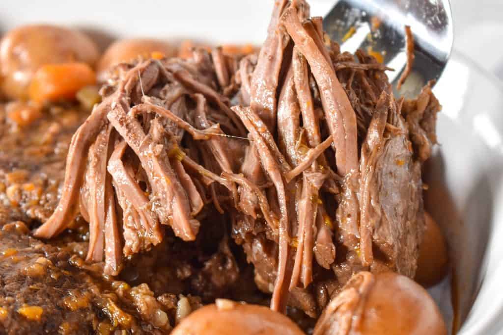 Pot roast that is fall apart tender being lifted by a serving fork.