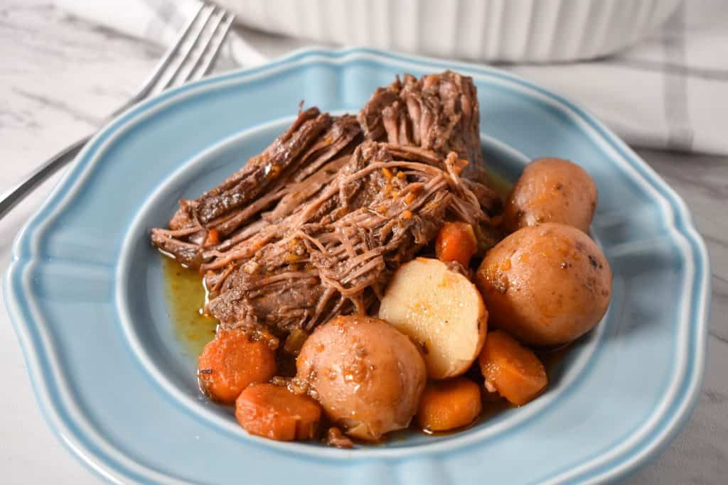 Pot roast served with carrots and small red potatoes on a light blue plate.