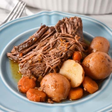 Pot roast served with carrots and small red potatoes on a light blue plate.