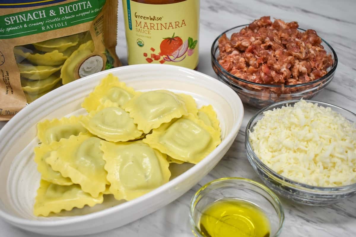 The ingredients for this ravioli bake prepped and arranged on a white surface.
