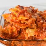 Ravioli bake being lifted by a large spoon from a glass casserole dish.