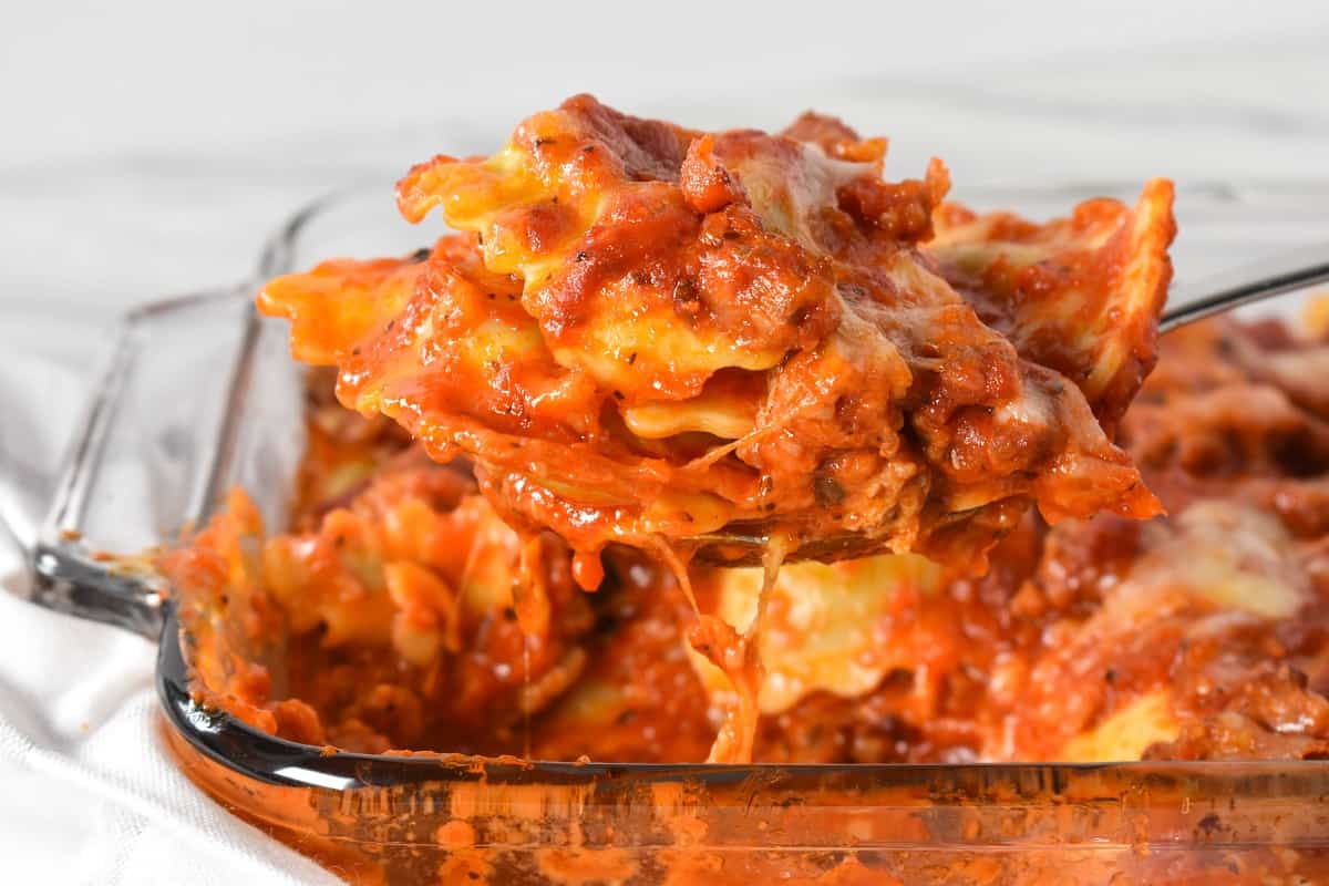 Ravioli bake being lifted by a large spoon from a glass casserole dish.