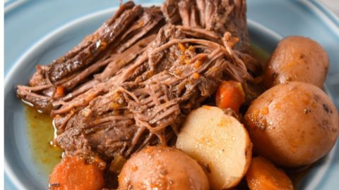 A piece of pot roast served with carrots and small red potatoes on a light blue plate.