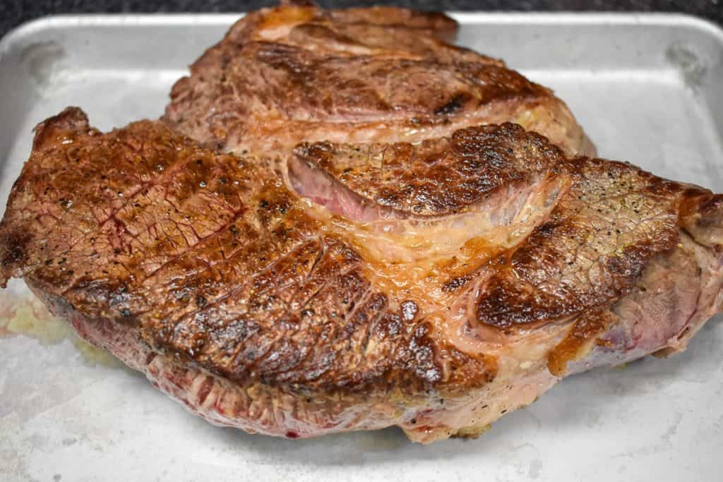 A large chuck pot roast that has been seared on both sides on a metal sheet pan.