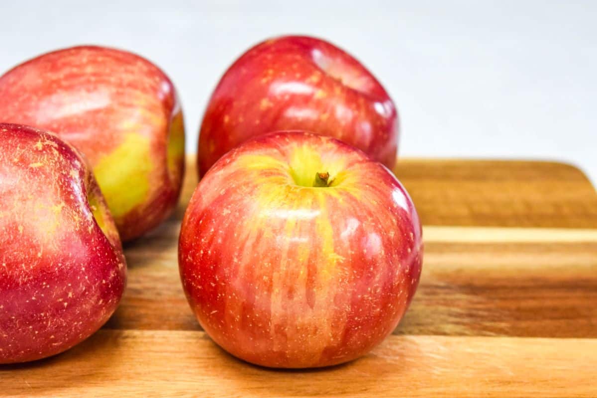 Four red apples on a wooden cutting board, ready to be peeled and sliced for cooking.