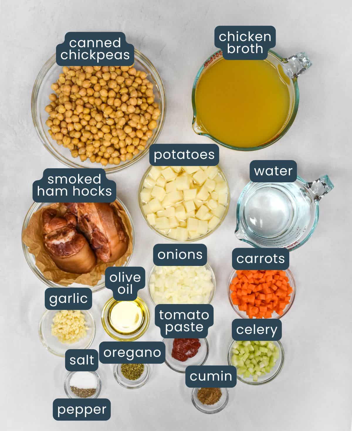 Overhead view of labeled ingredients for soup, including chickpeas, smoked ham hocks, vegetables, and spices.