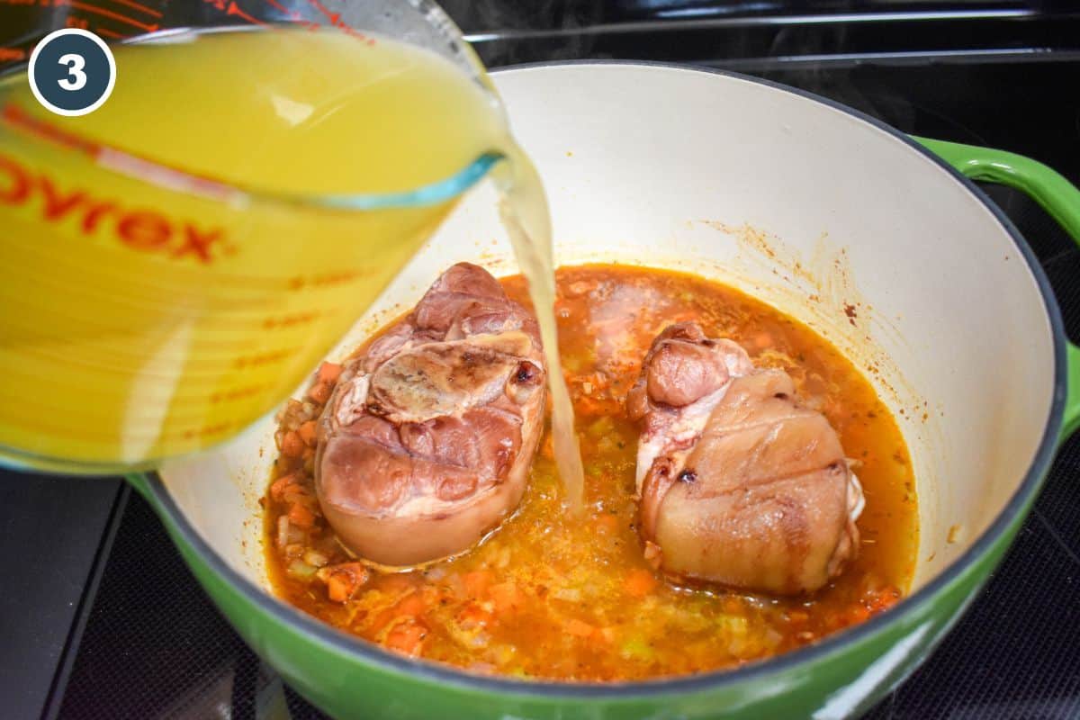 Chicken broth being poured into the pot over smoked pork shanks.
